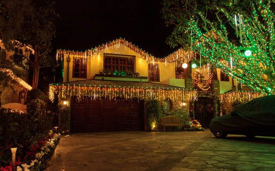 A house is decorated with christmas lights and a car is parked in front of it.