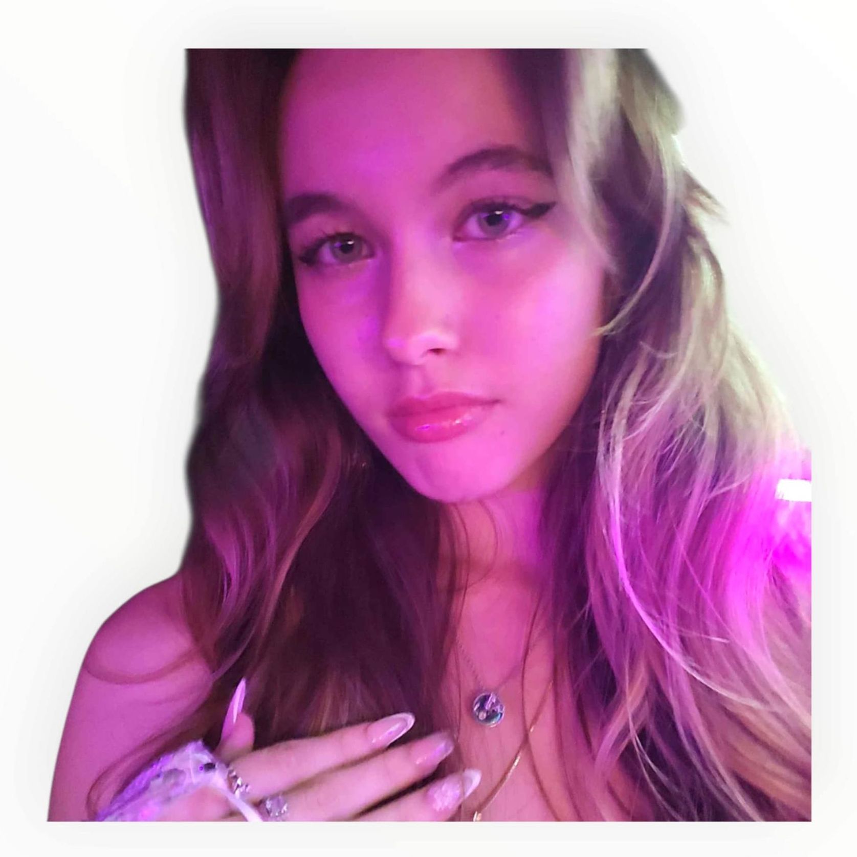 Woman with long brown hair and a pink-purple glow, looking towards the camera. She wears a necklace and has long nails.