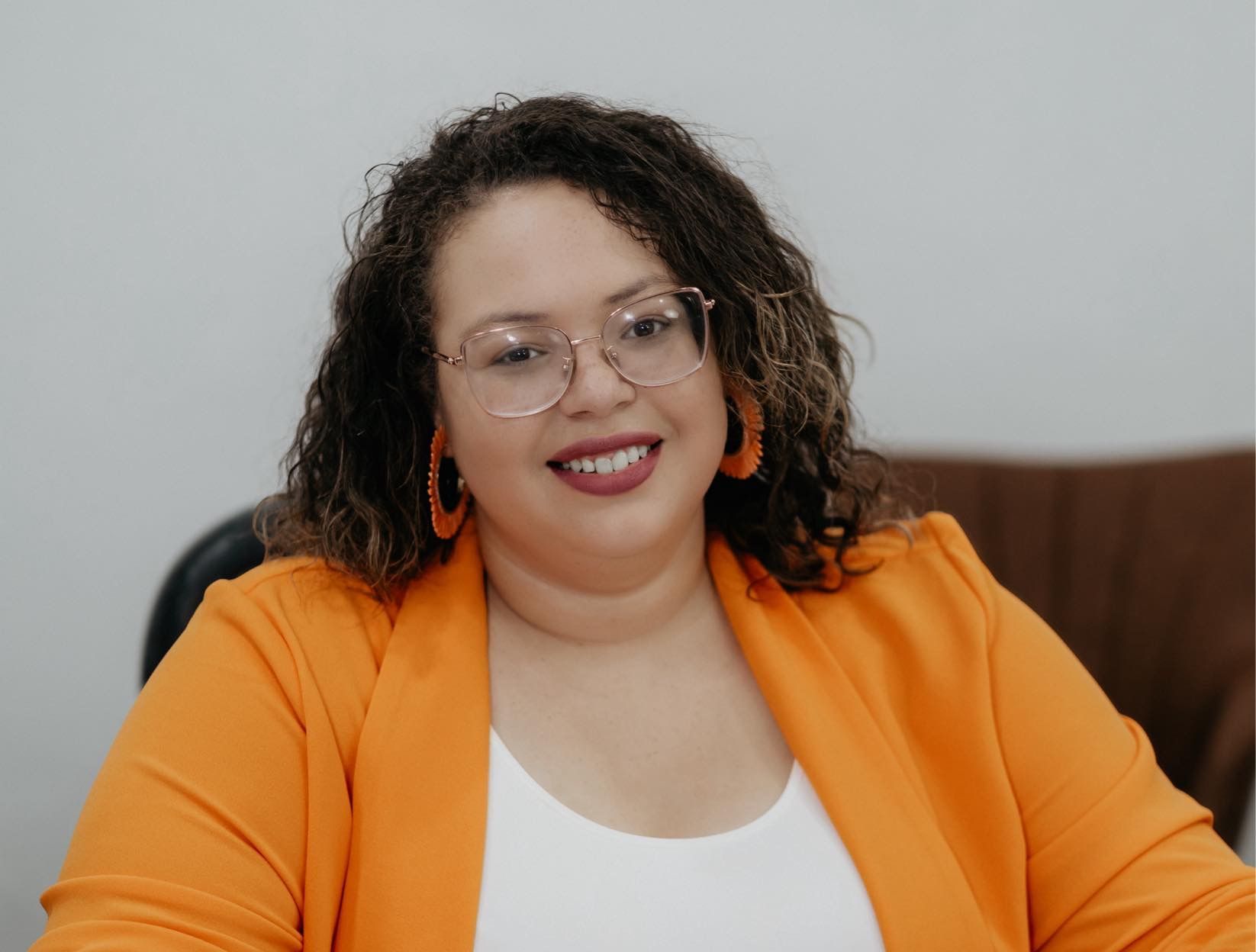 A woman wearing glasses and an orange jacket is smiling for the camera.