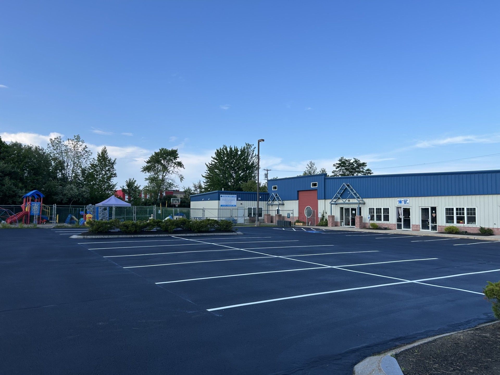 A building with a playground and a large parking lot under a blue sky.