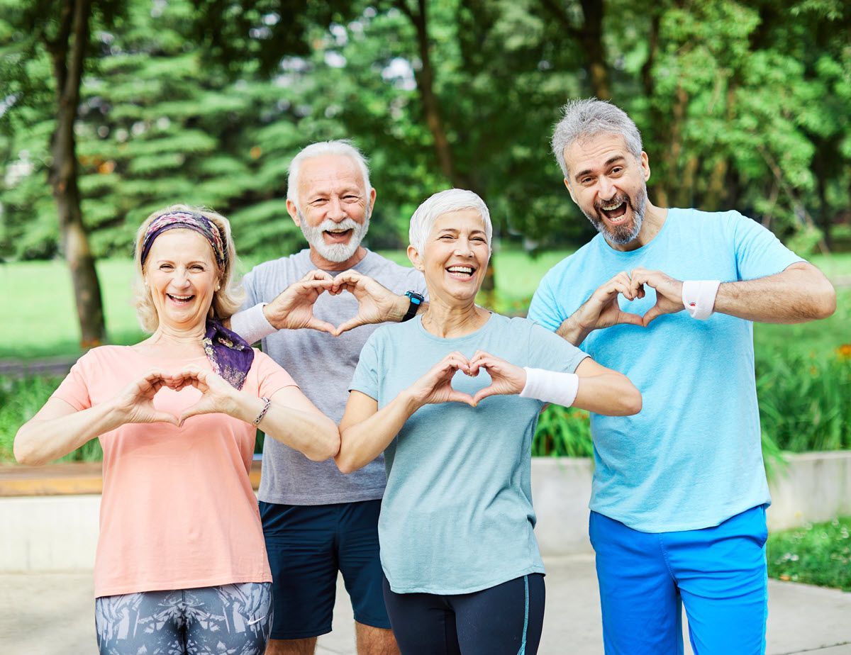Four smiling people outdoors making heart shapes with their hands in a green park.