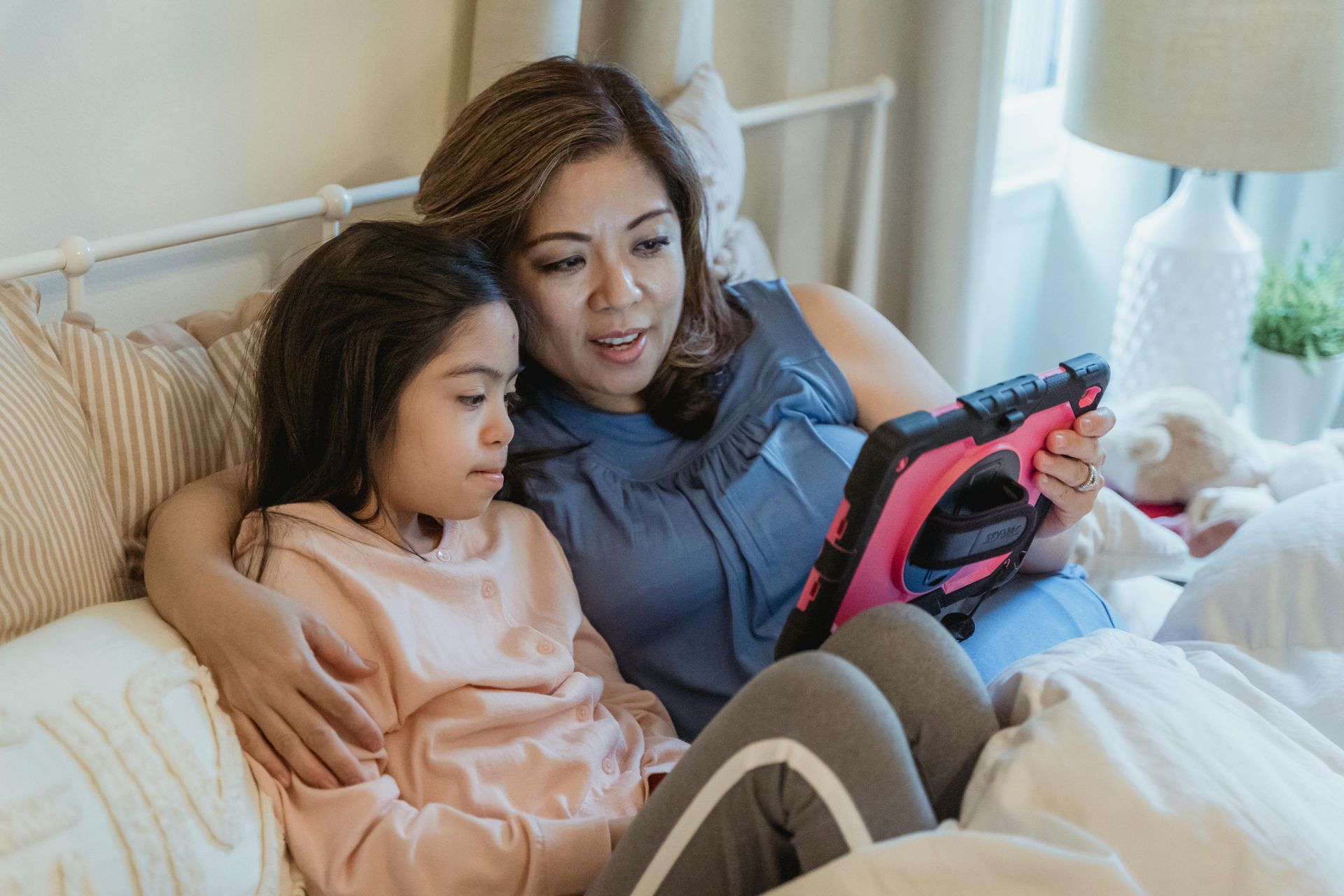 Woman and child relaxing on a bed while looking at a tablet together.