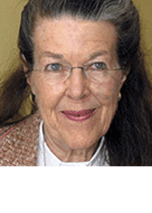 Woman with glasses, smiling, wearing a white shirt and tweed jacket.