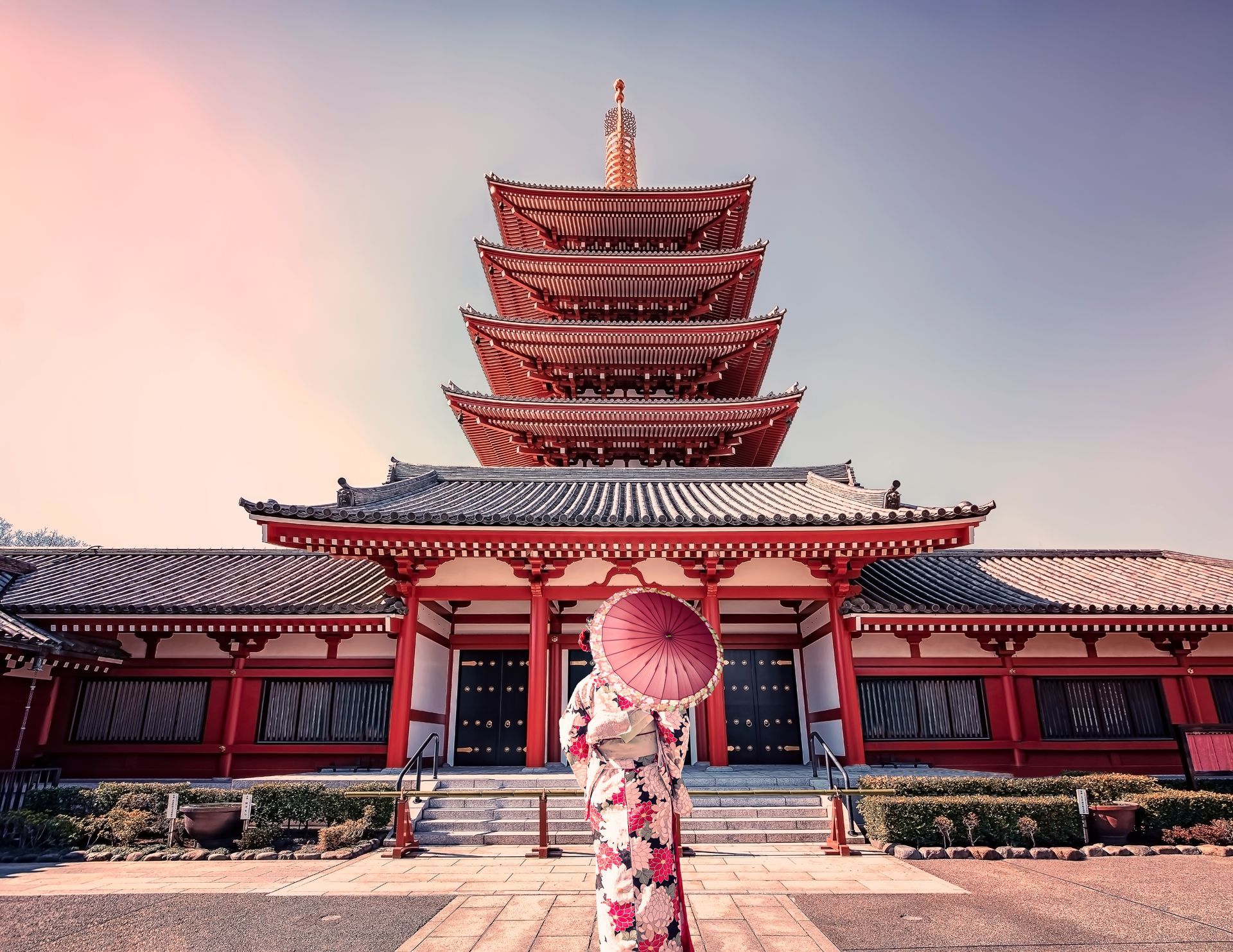 A woman in a kimono is standing in front of a temple holding an umbrella.