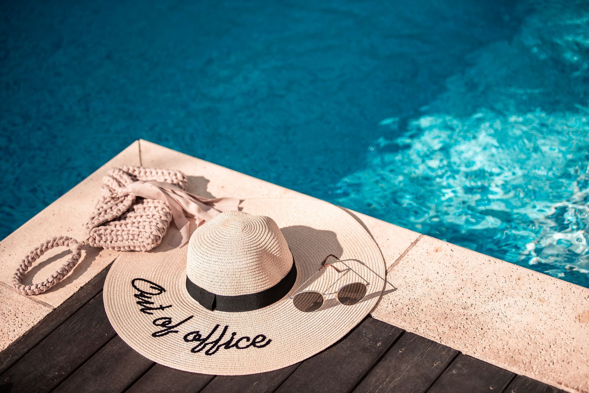 A hat and sunglasses are sitting on the edge of a swimming pool.