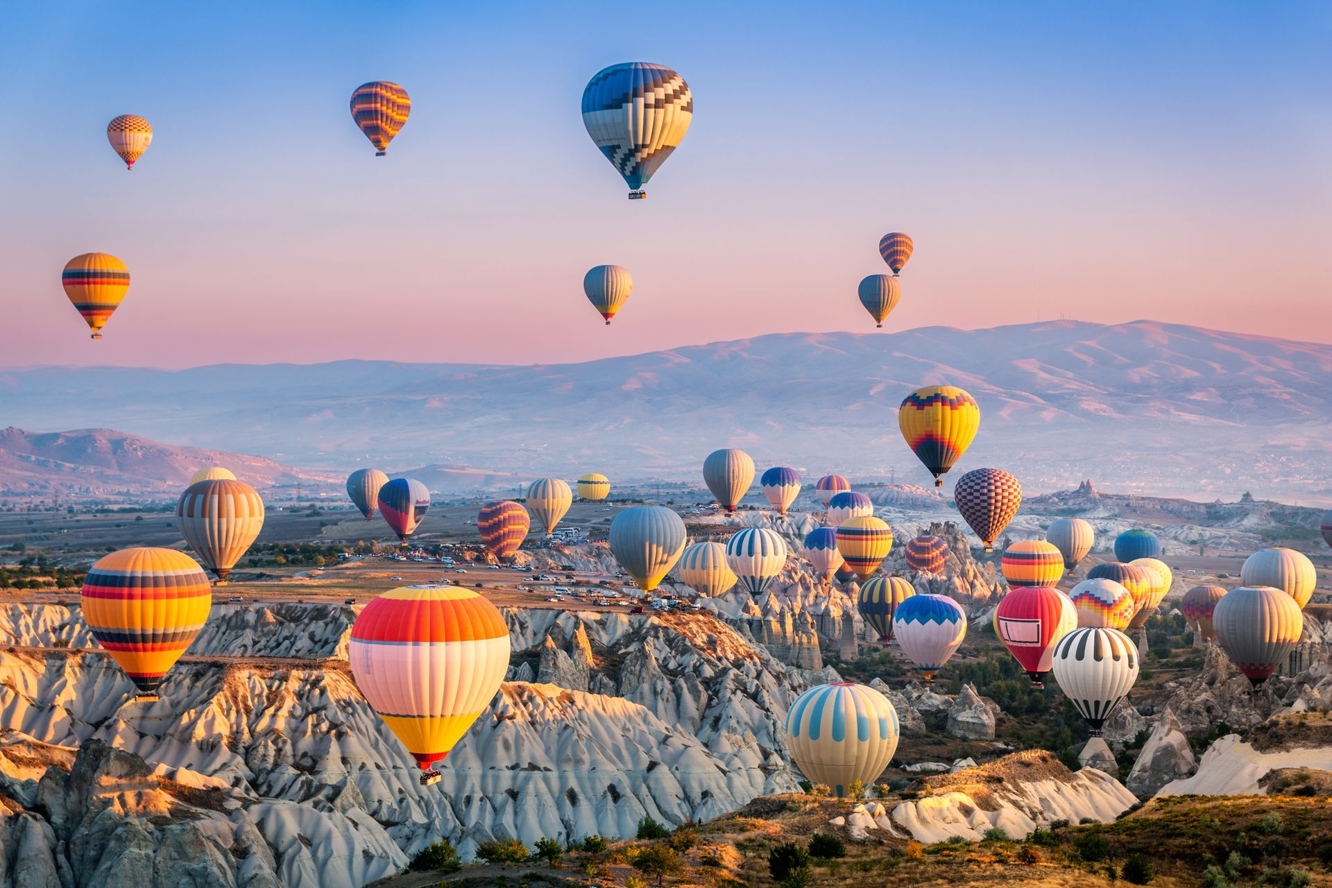A bunch of hot air balloons are flying over a valley.