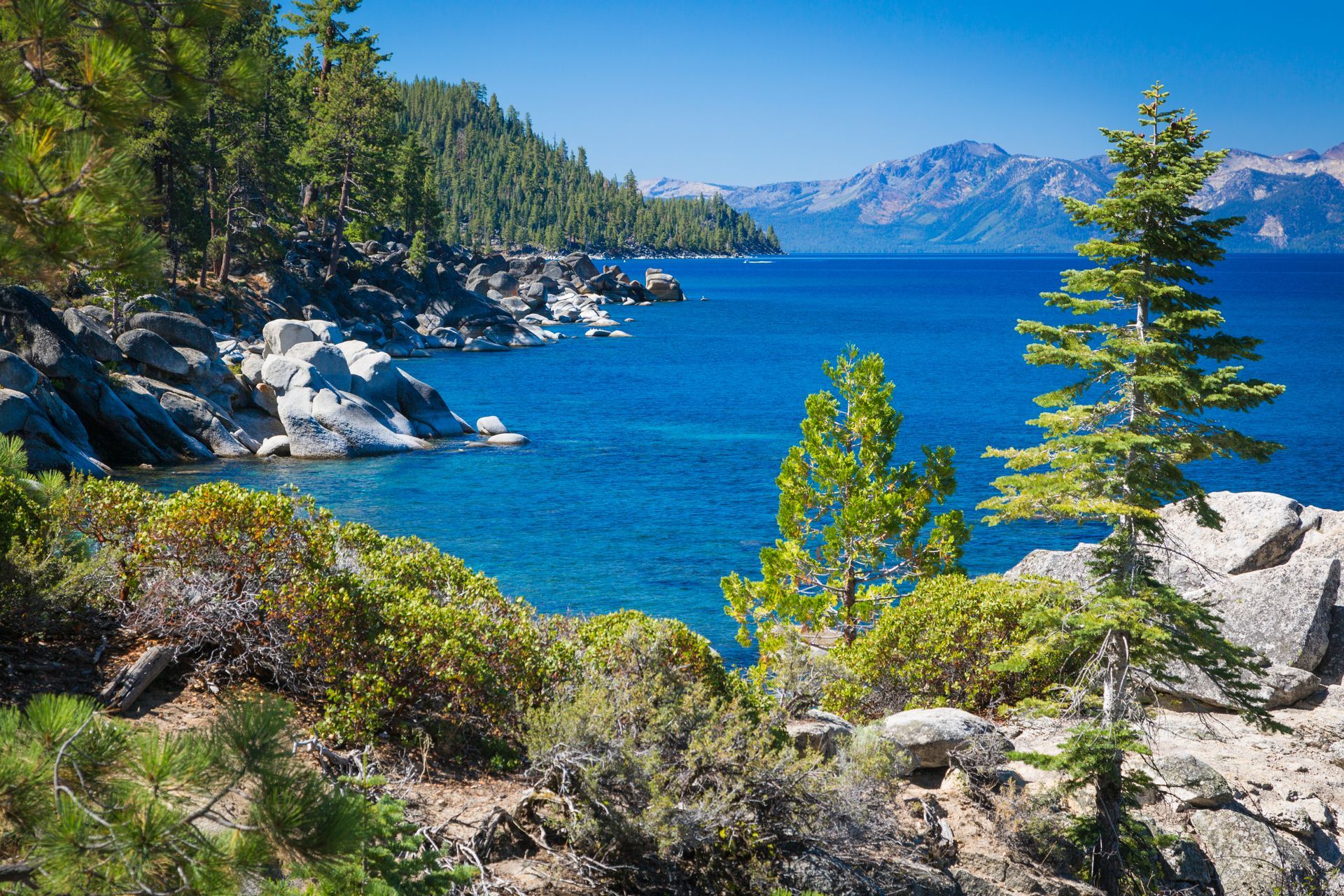 A lake surrounded by trees and rocks with mountains in the background