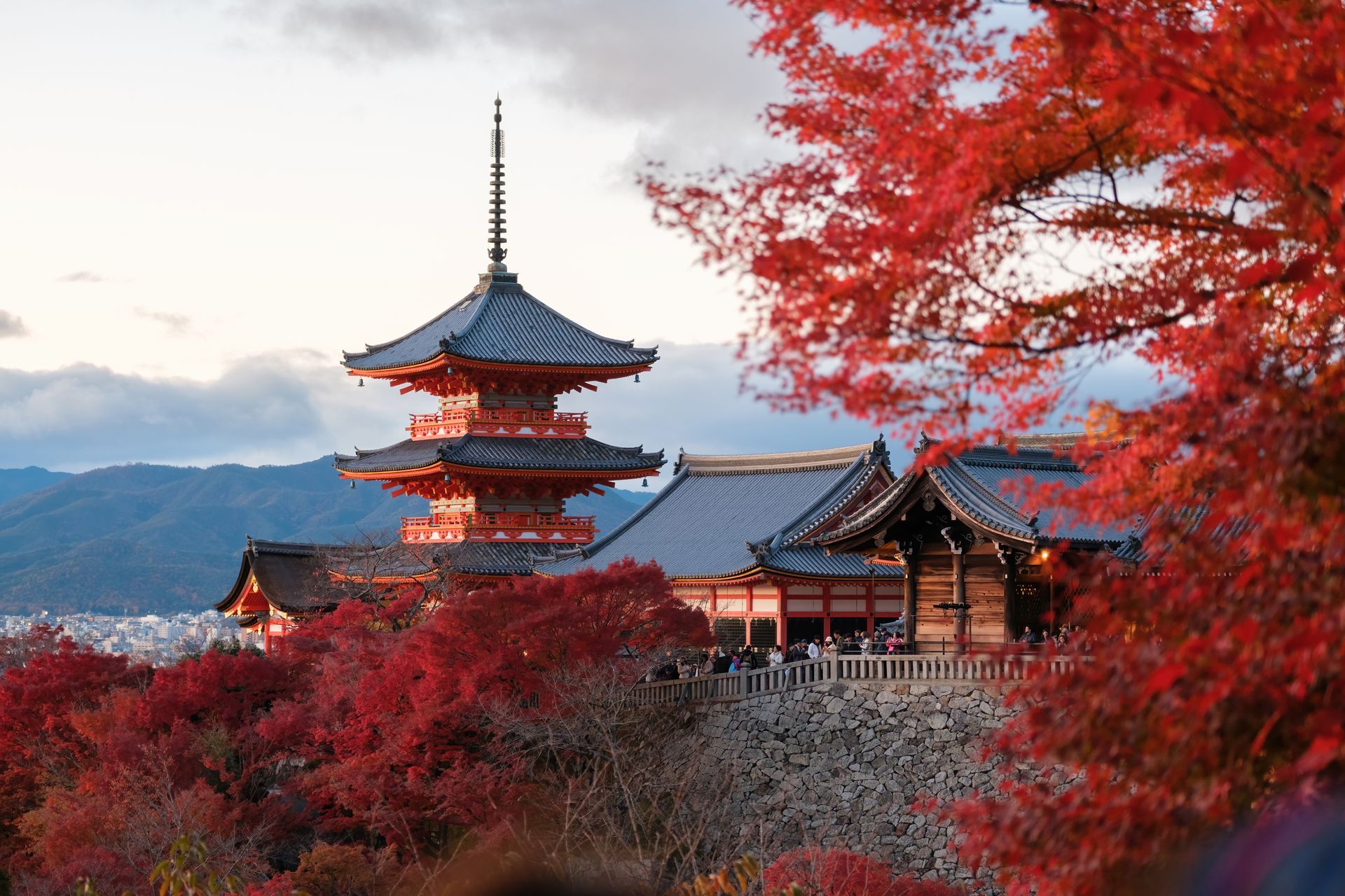 A pagoda is surrounded by trees with red leaves and mountains in the background.