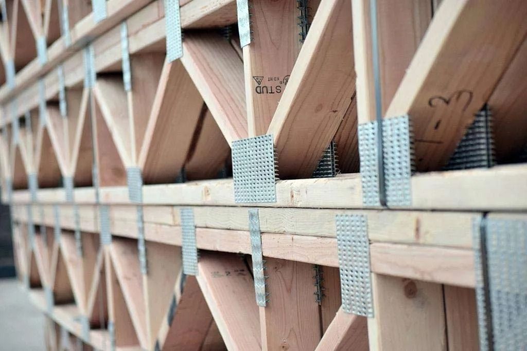 A stack of wooden roof trusses reinforced with metal connector plates, viewed from a close-up, angled perspective.