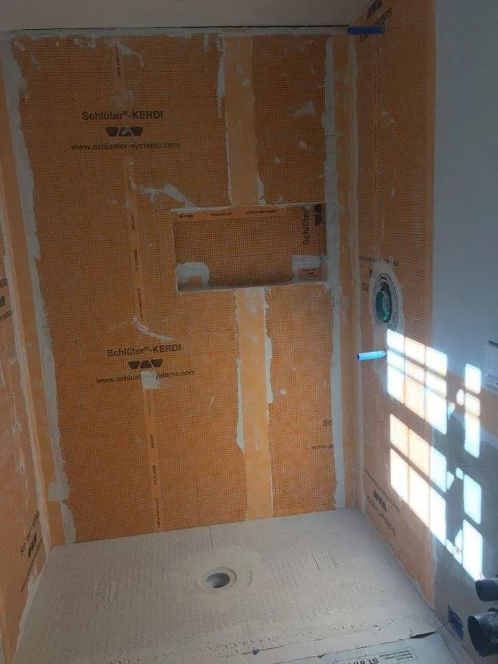 A shower stall under construction with orange waterproof membrane on walls, a built-in recessed niche, and a shower pan.