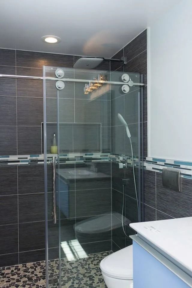 Modern bathroom with dark tiled shower, glass sliding door, handheld sprayer, and a white vanity in the foreground.