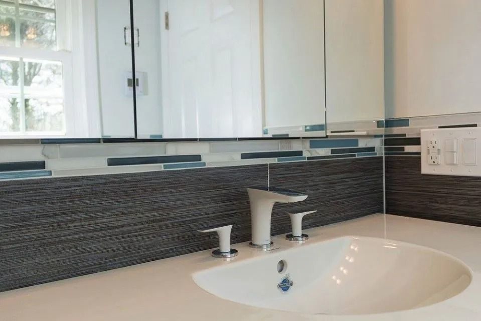A modern bathroom sink with a white faucet, dark wood-textured backsplash, and blue glass accent tile below a mirror.