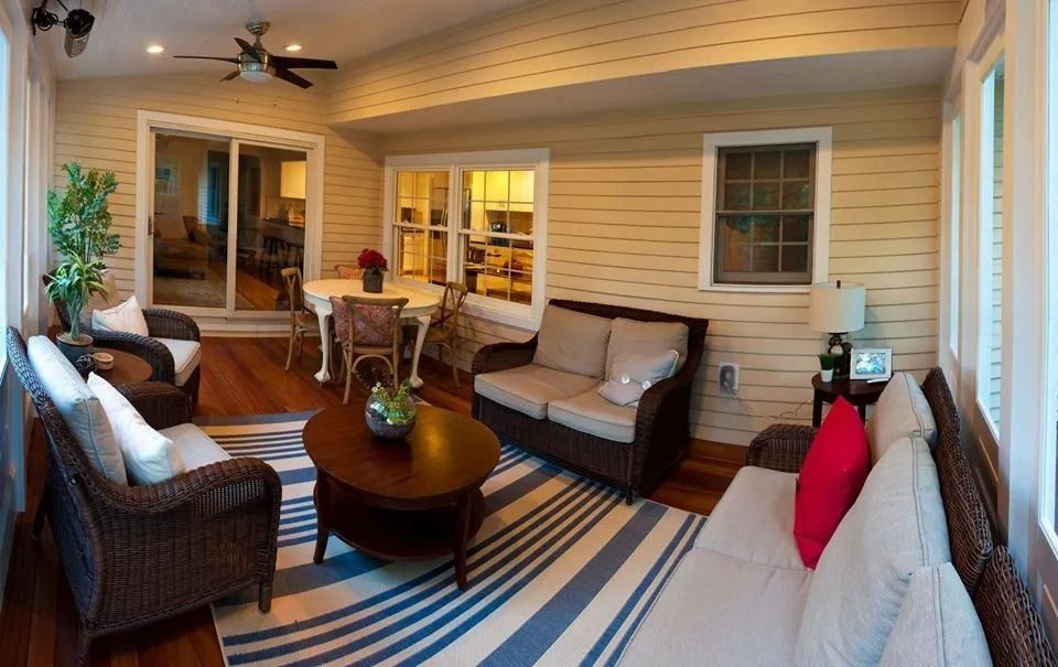 A sunroom featuring wicker furniture, a round wooden coffee table, and a blue-and-white striped rug on wood floors.