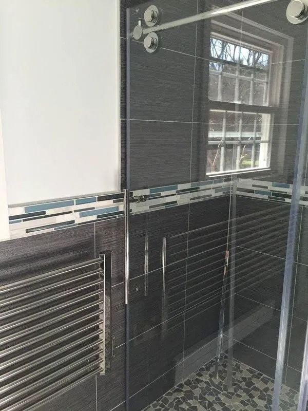 A modern bathroom shower area featuring dark grey wall tiles, a multi-colored accent stripe, and a glass sliding door.