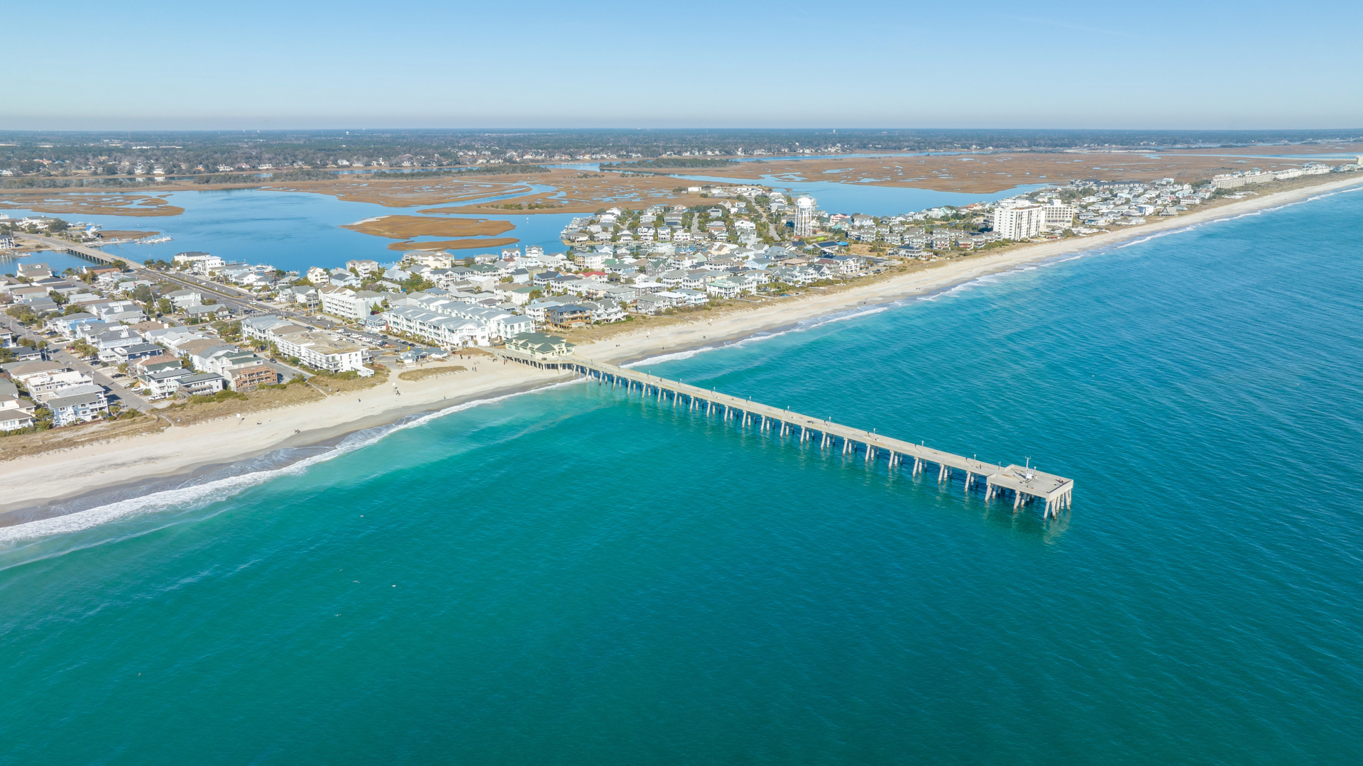 An aerial view of a pier leading into the ocean with a city in the background.