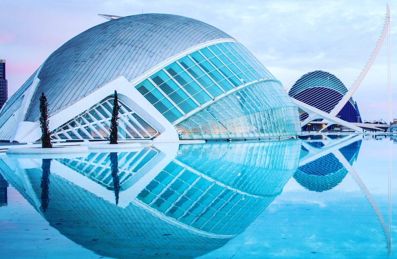 Futuristic glass-domed buildings reflected in calm blue water under a clear sky