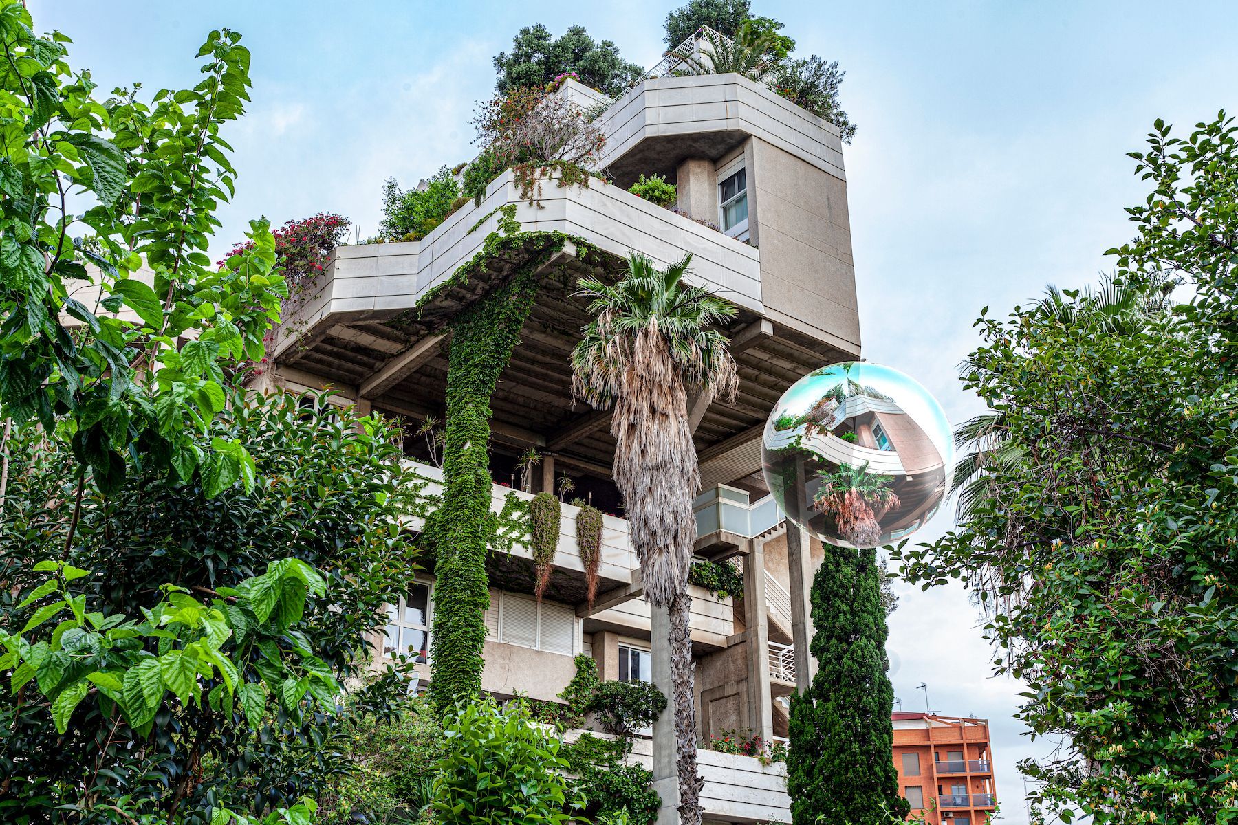 Modern concrete house with lush greenery and a reflective sphere sculpture outside