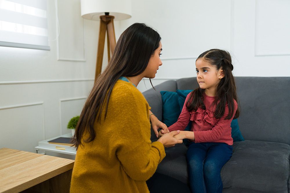 A woman is holding a little girl 's hand while sitting on a couch.