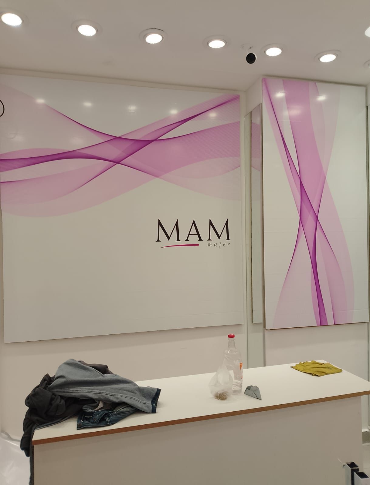 Pared blanca y rosa con un escritorio y ropa. Interior de tienda con el logo