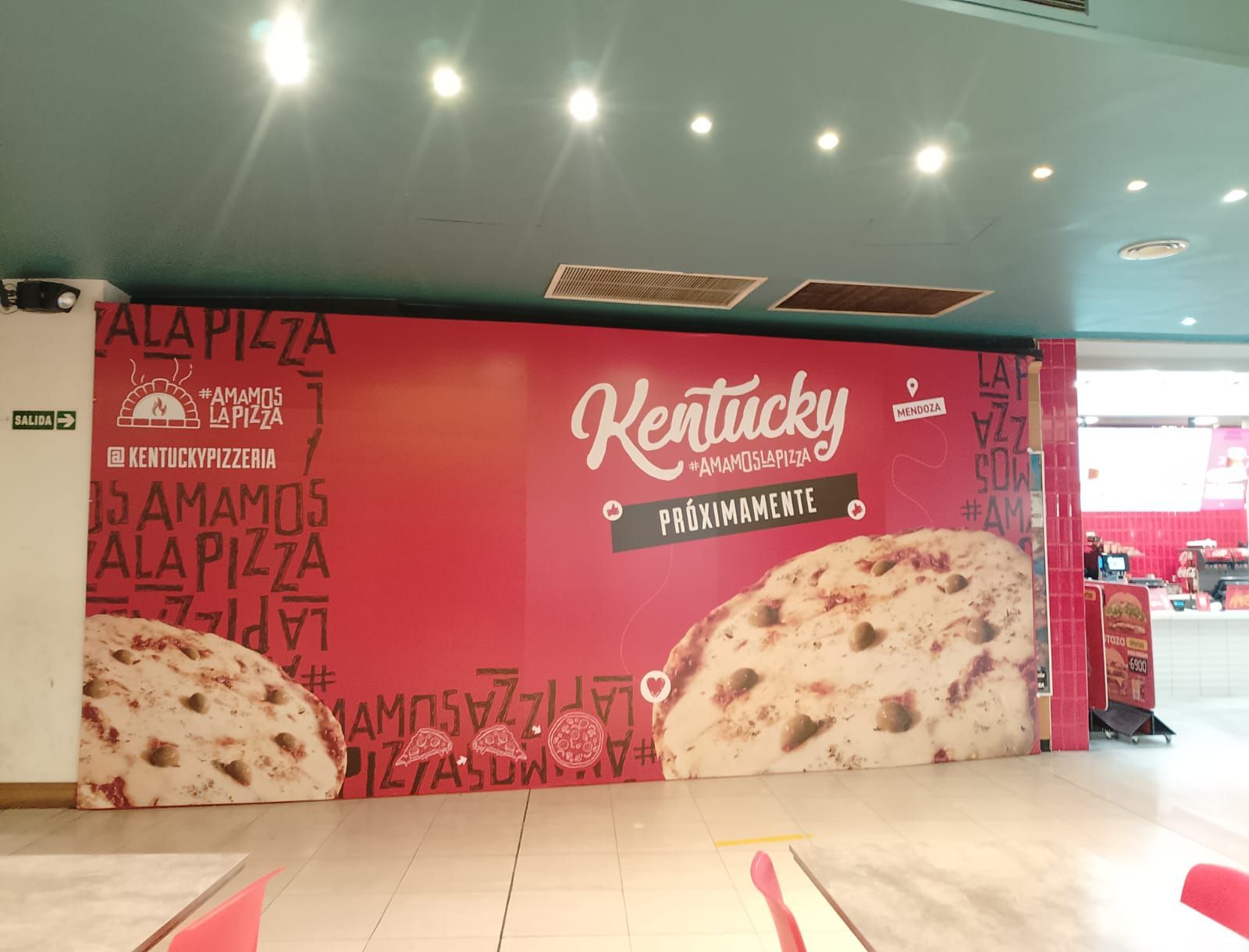 Anuncio de pizza Red Kentucky en un entorno interior con un techo verde azulado.