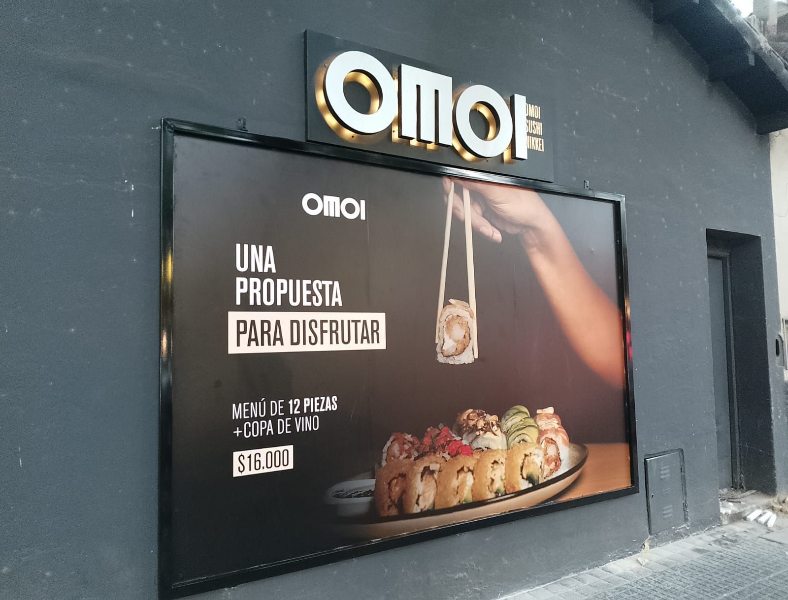 Letrero de restaurante de sushi con logotipo iluminado y un anuncio oscuro