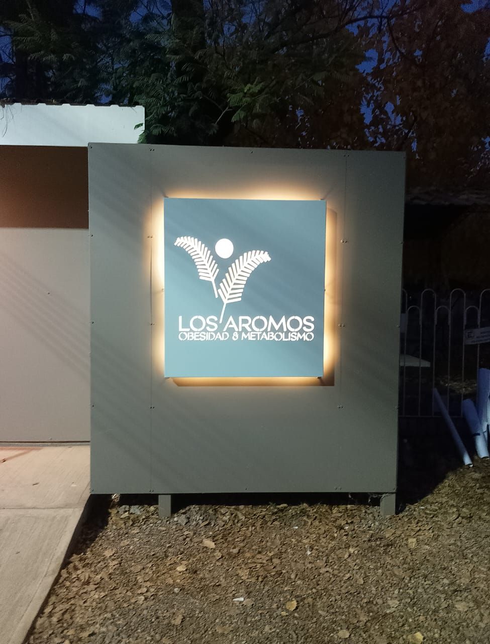 Letrero para restaurante “Los Aromos”, cuadrado turquesa con borde iluminado, montado sobre panel gris.