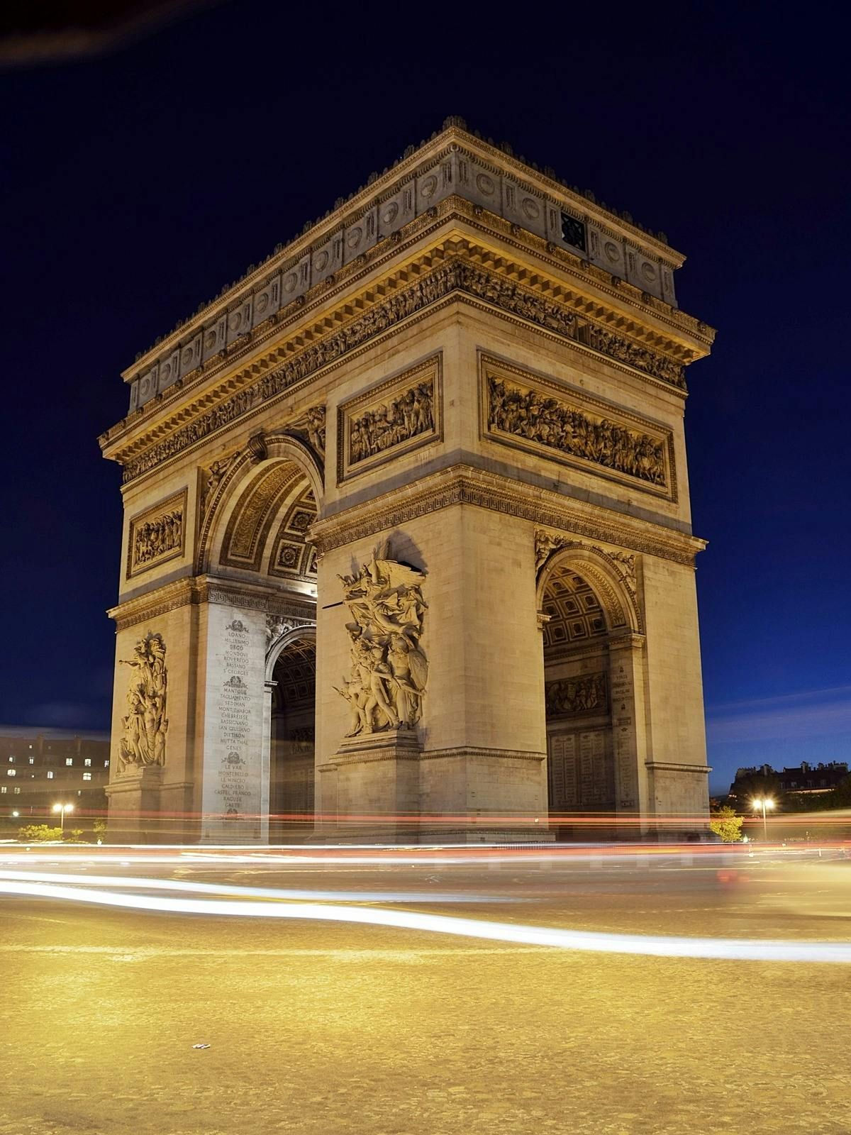 Arc de Triomphe, Paris, at night; headlights streak by the monument.