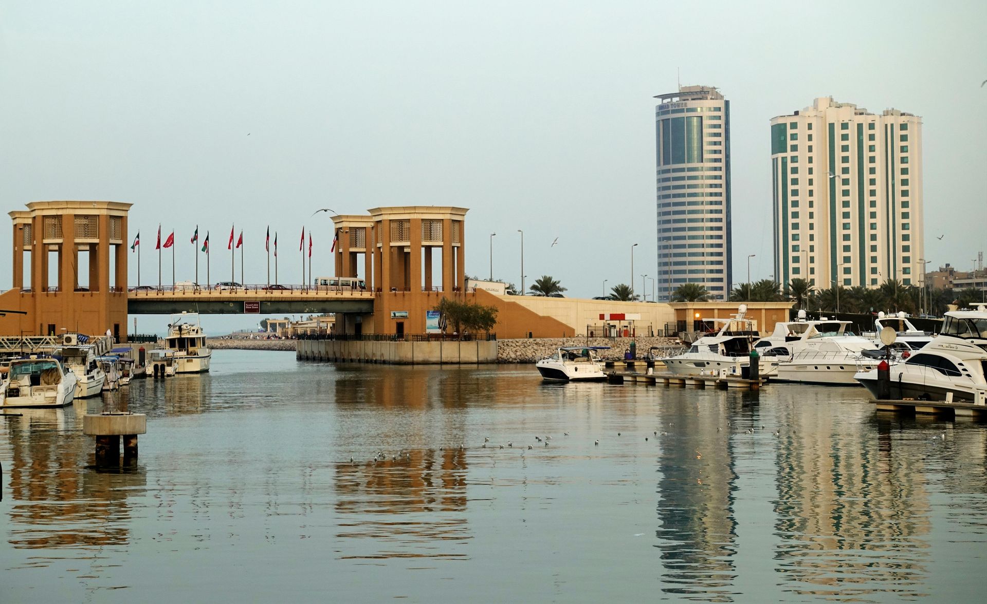 Waterfront scene with boats, a bridge, and tall buildings under a cloudy sky.