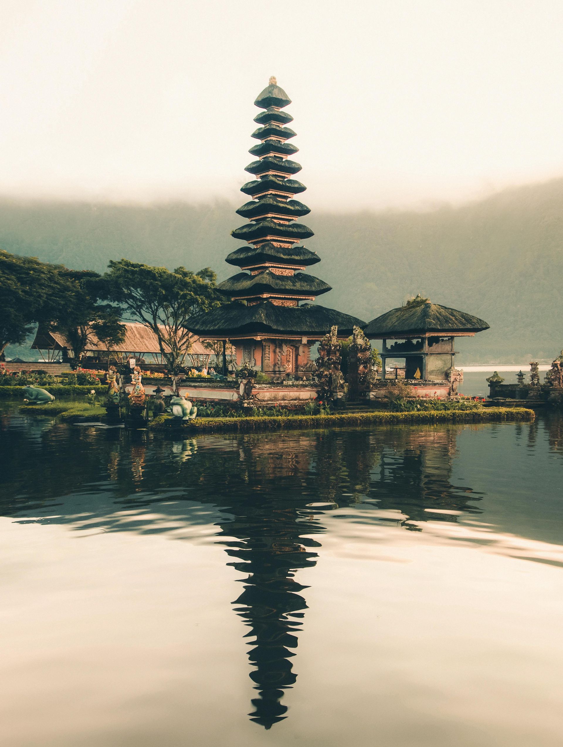 Temple on a lake reflects its tiered structure in still water against a misty mountain backdrop.