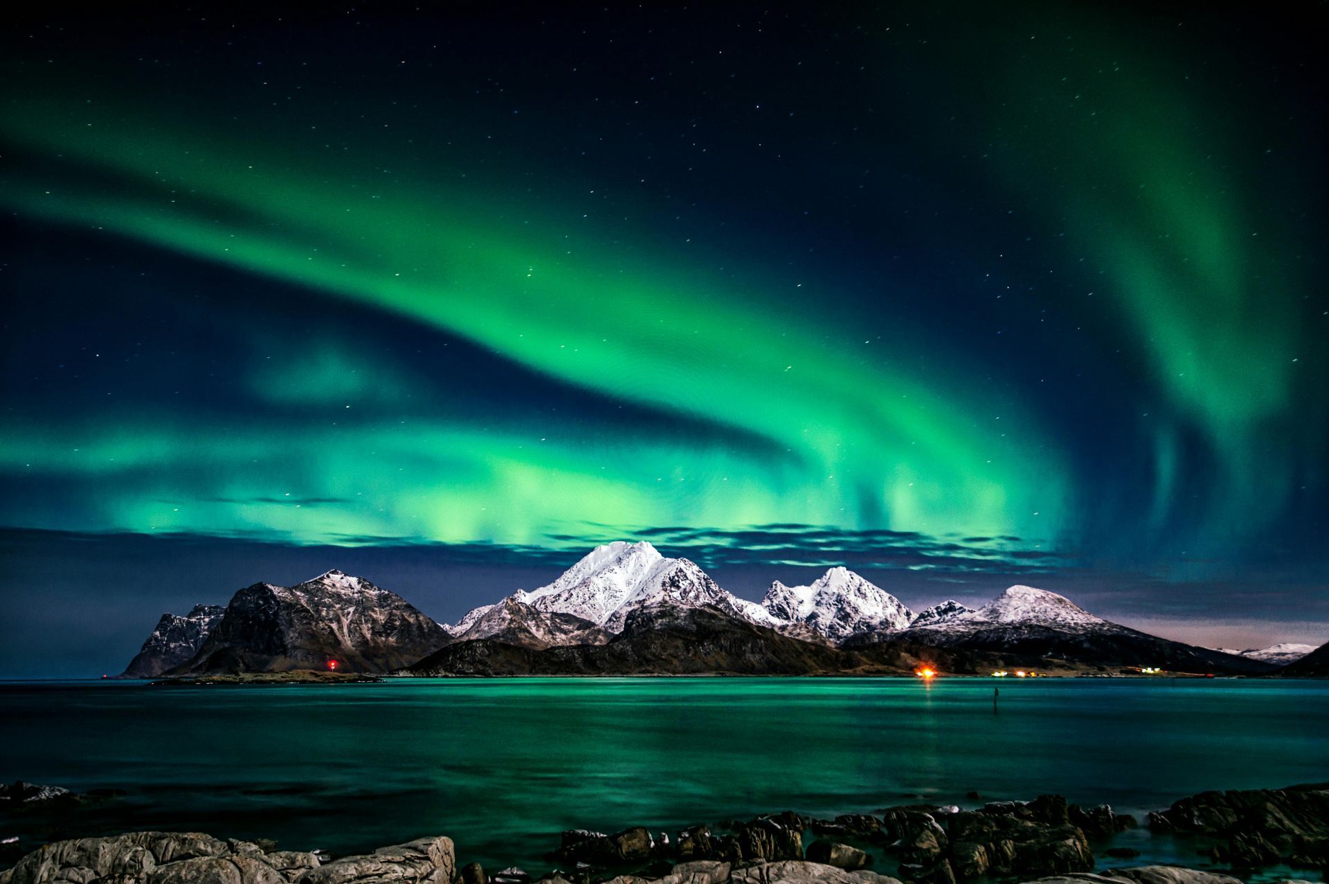 Green aurora borealis over snow-capped mountains and water at night.
