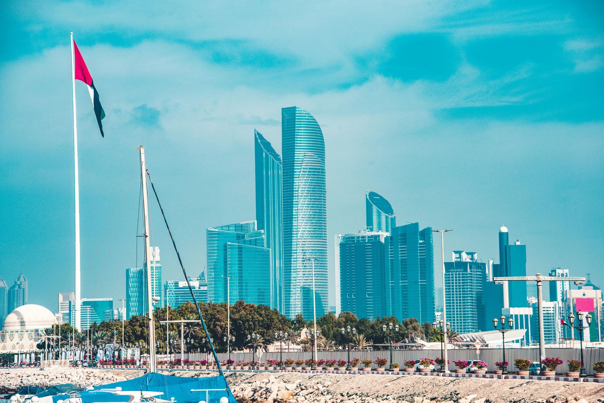 Abu Dhabi skyline with UAE flag against a blue sky, featuring modern skyscrapers.