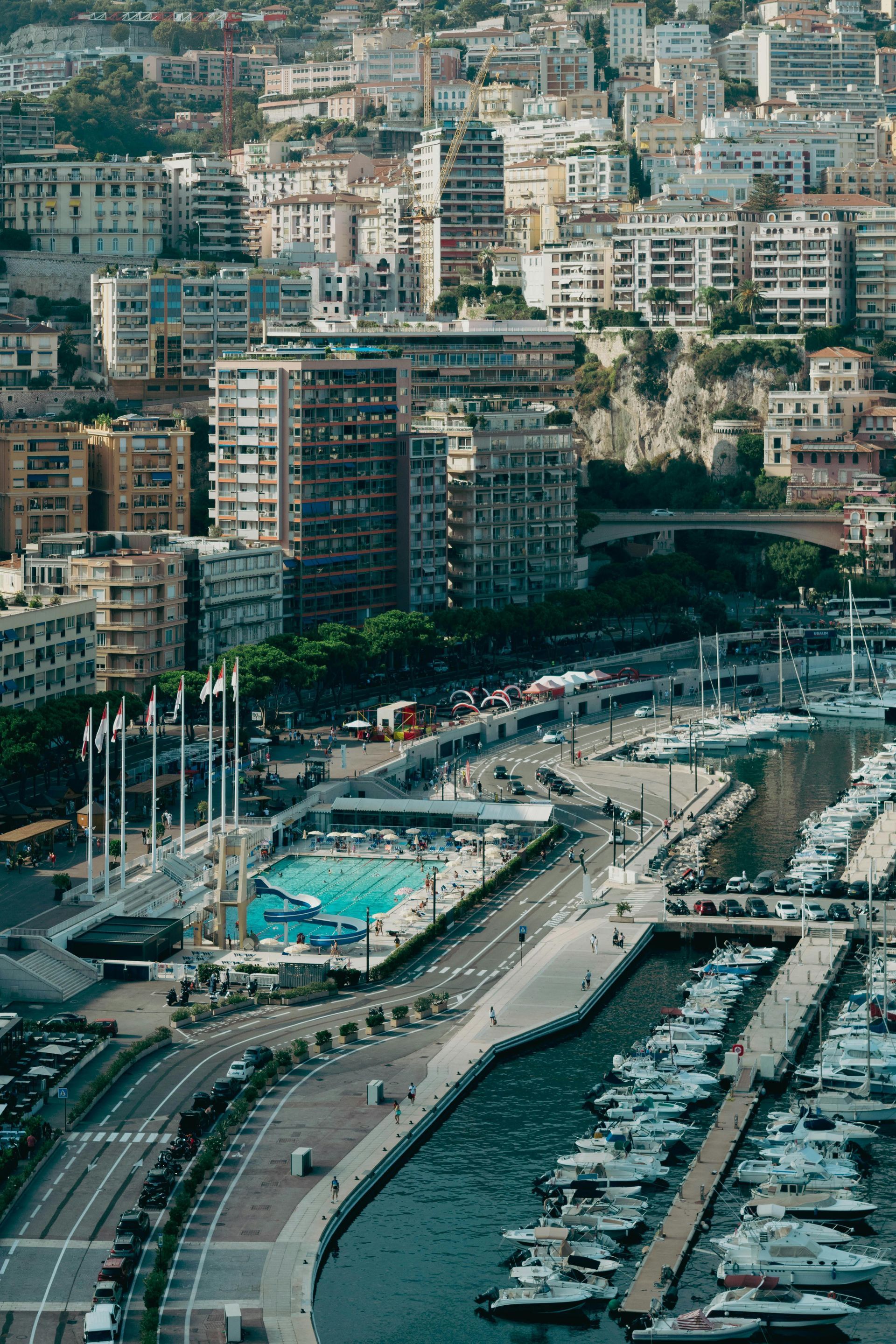 View of Monaco with boats docked in the harbor, buildings on a hillside, and a pool.