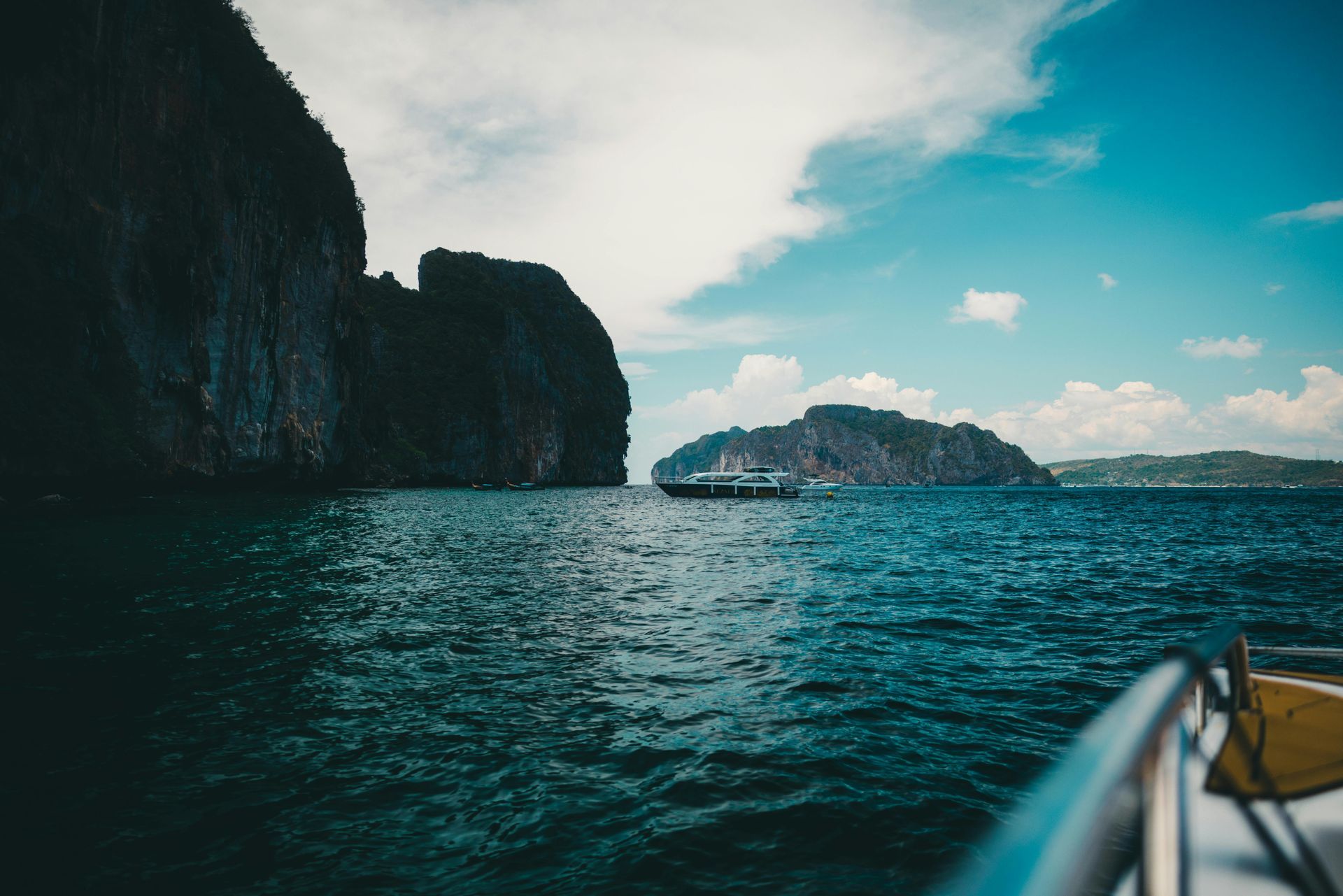 Ocean view with dark cliffs, turquoise water, and a boat. Cloudy sky.