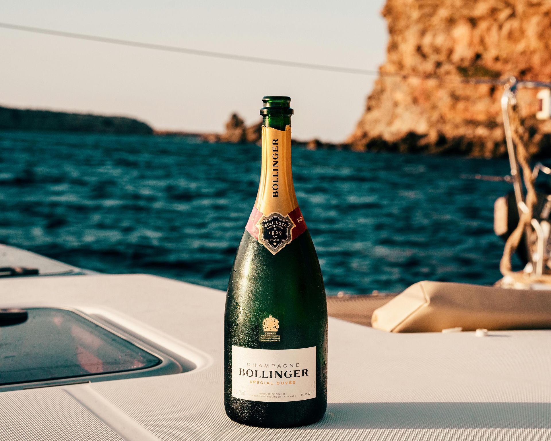 Champagne bottle on a boat with ocean and cliffs in background.