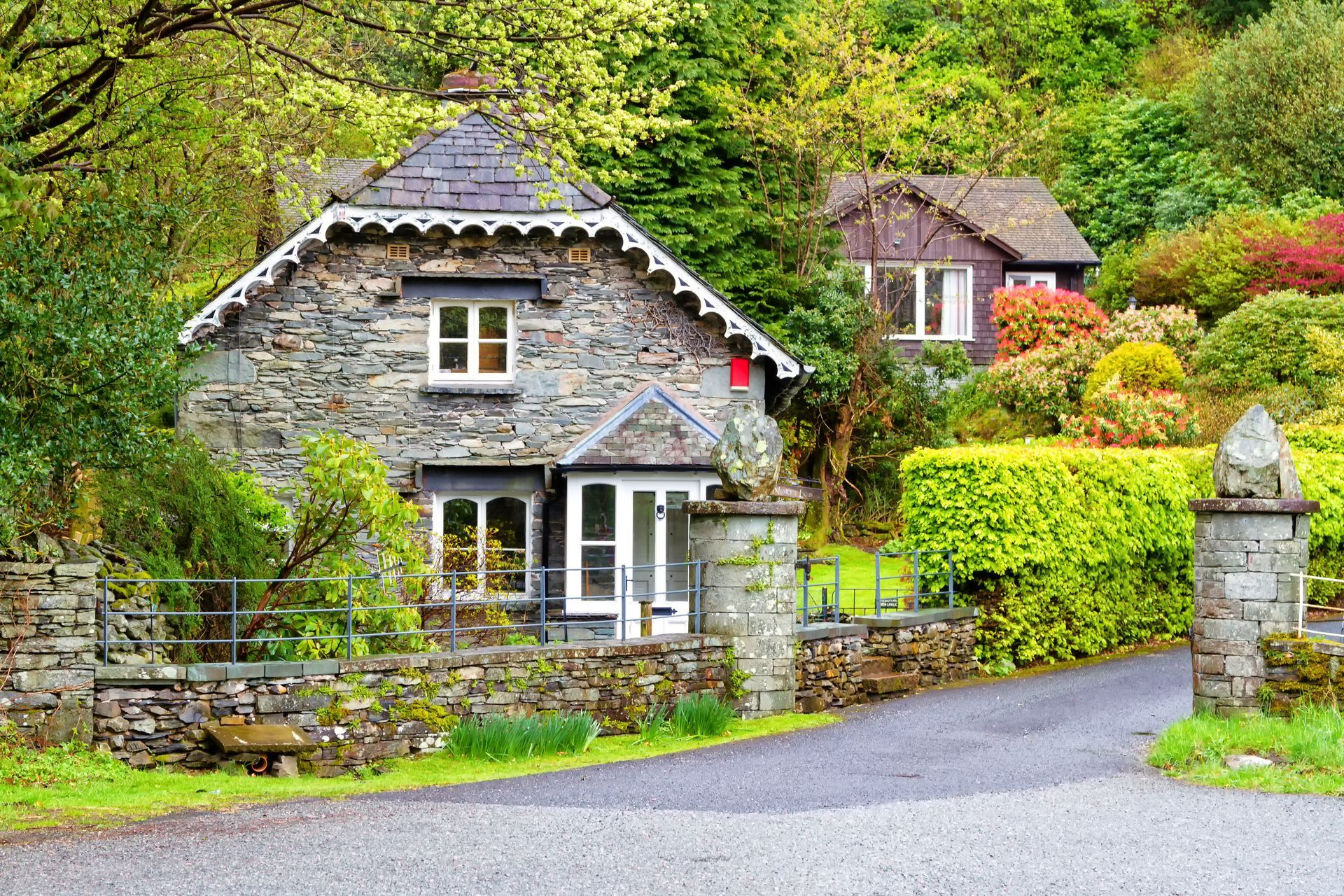 Stone cottage with slate roof and white trim in a lush, green setting; another cottage in the background.
