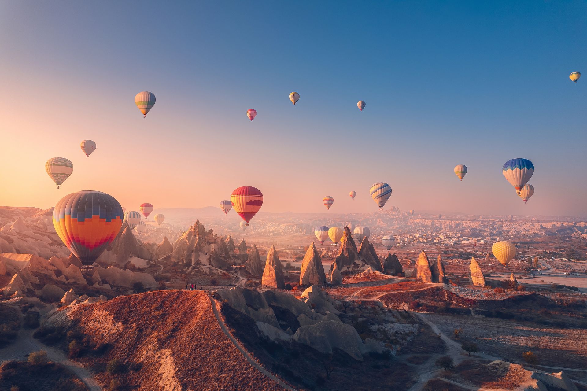 Hot air balloons drift over unique rock formations at sunrise in Cappadocia, Turkey.
