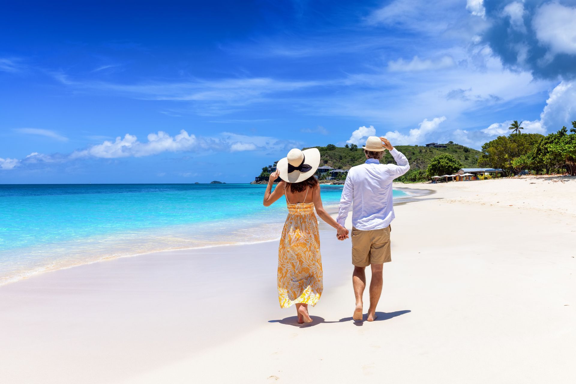 Couple walking hand-in-hand on a white sand beach, turquoise water, blue sky, sunny day.