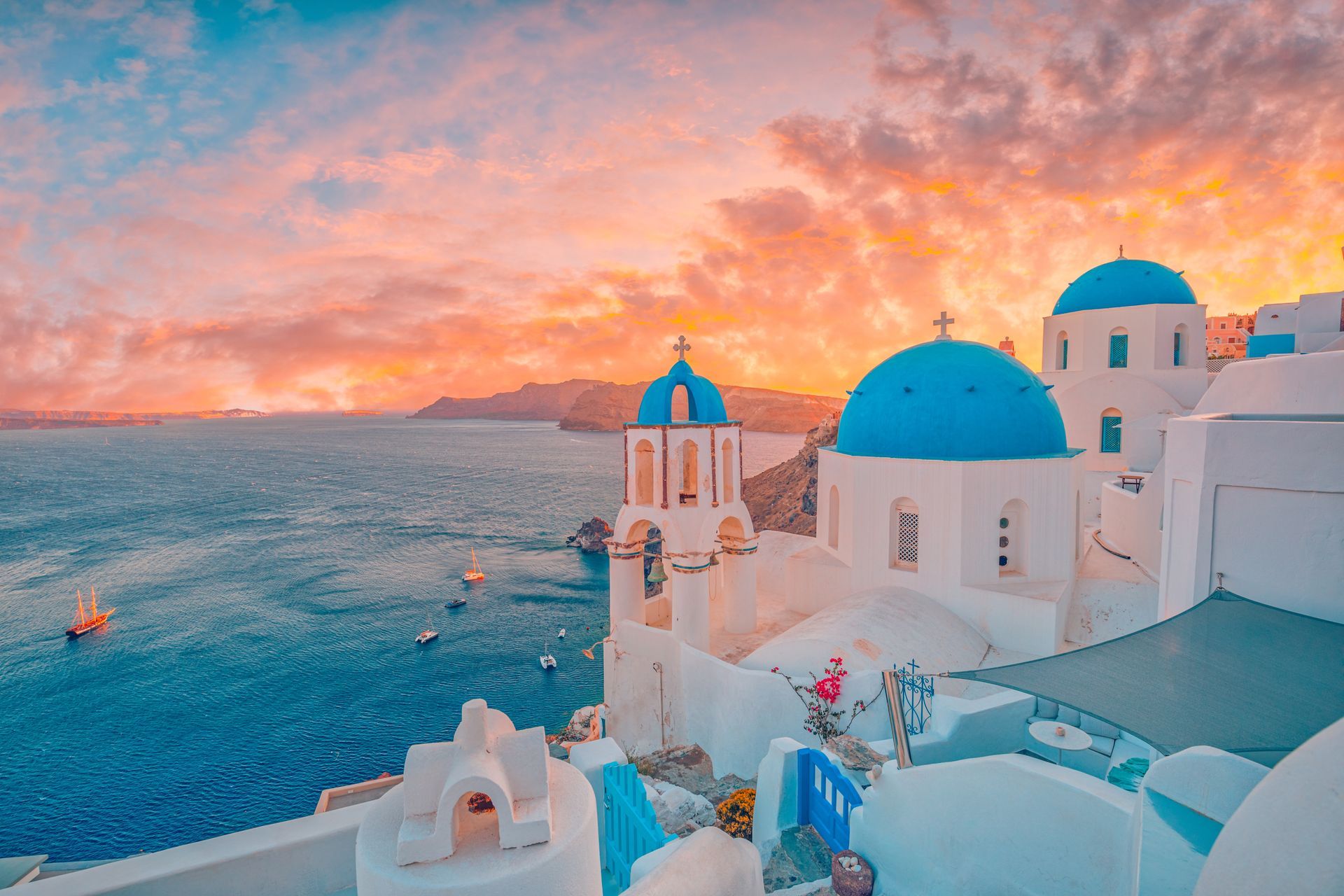 White buildings with blue domes in Santorini, Greece, at sunset with a colorful sky over the Aegean Sea.