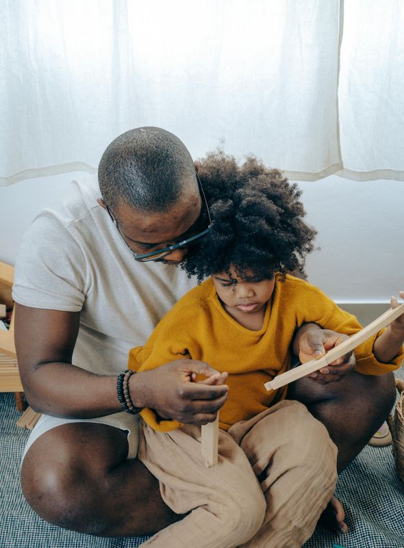 A man and a child are sitting on the floor reading a book together.