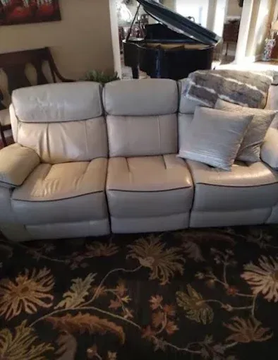 A white leather couch is sitting in a living room next to a piano.