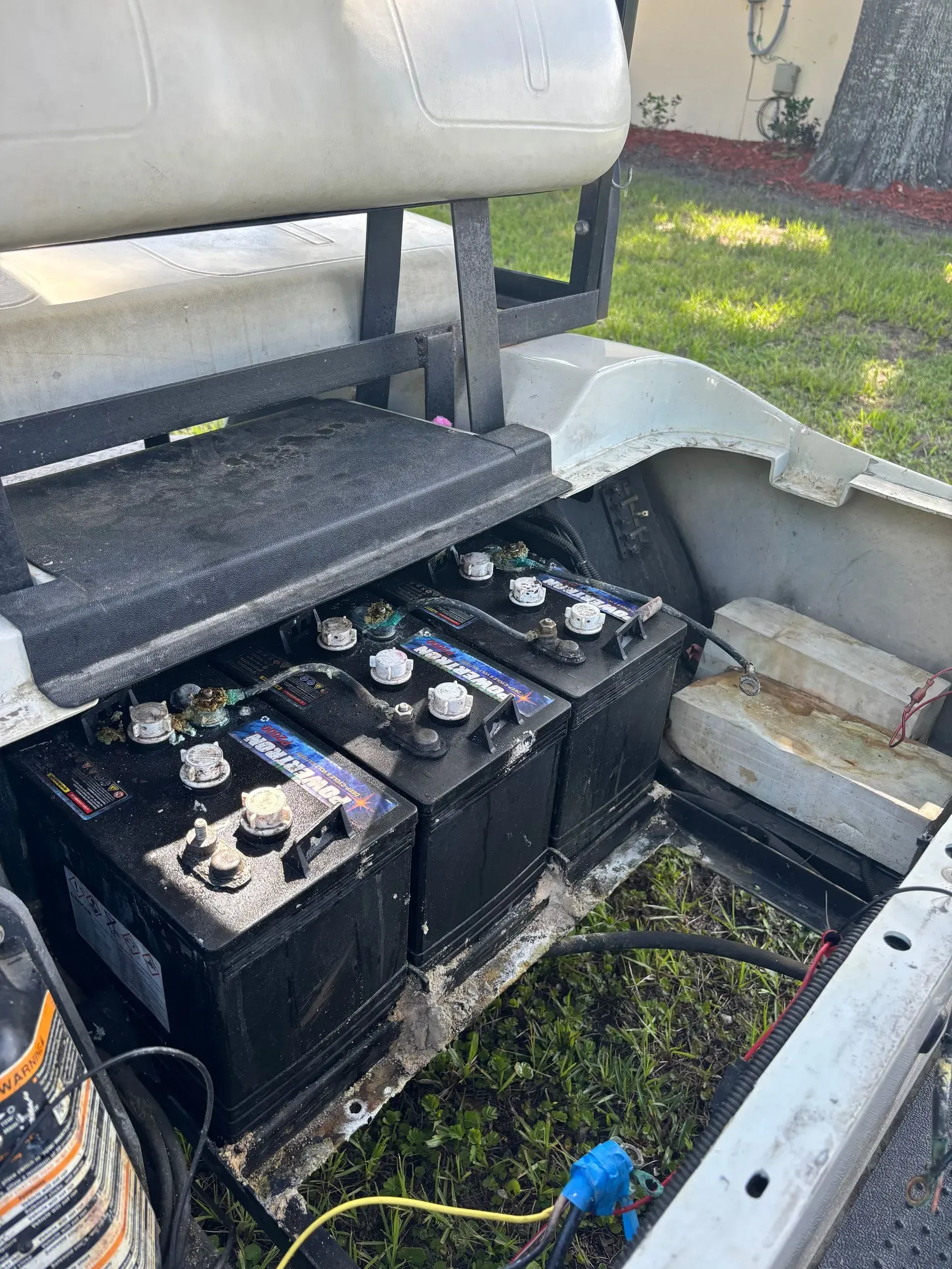 Golf cart battery compartment with three black batteries, electrical cables, and a blue connector.
