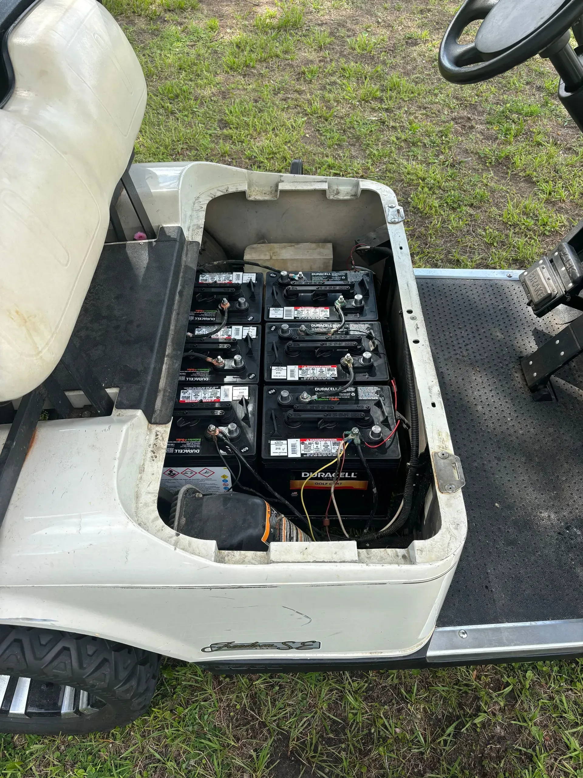 Golf cart with open battery compartment filled with batteries, on grass.