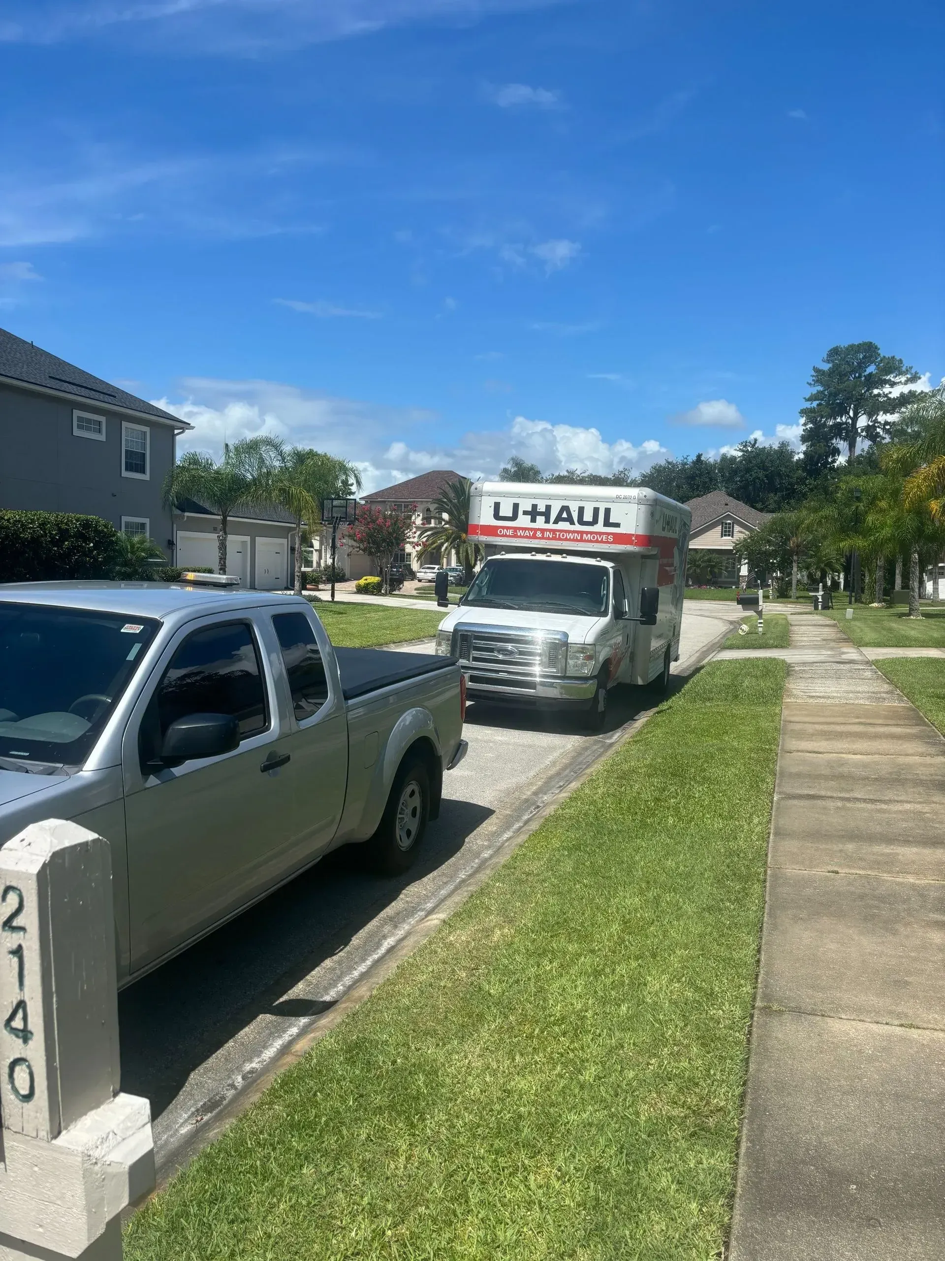 U-Haul truck parked on a residential street next to a gray pickup truck, near a house with the number 2140.