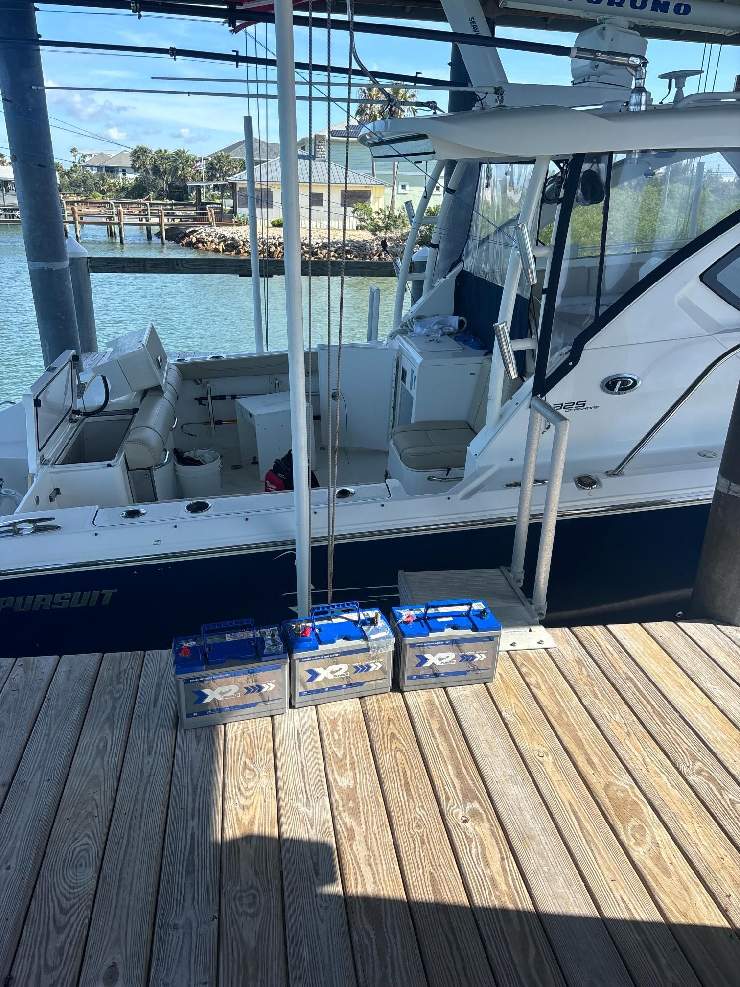Three blue boat batteries on a dock in front of a white and blue boat.