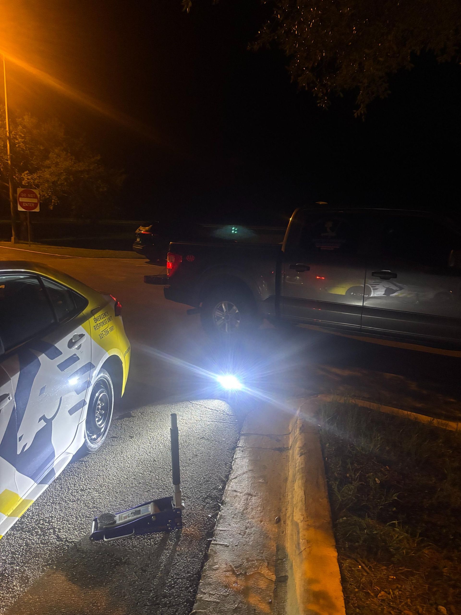 A nighttime scene with a yellow car, a truck, and a bright light illuminating the roadside.