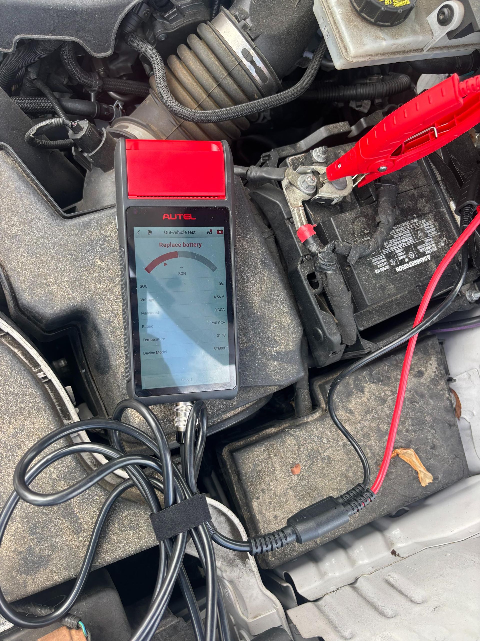 Battery tester connected to a car battery under the hood. Red and black wires attached to terminals.