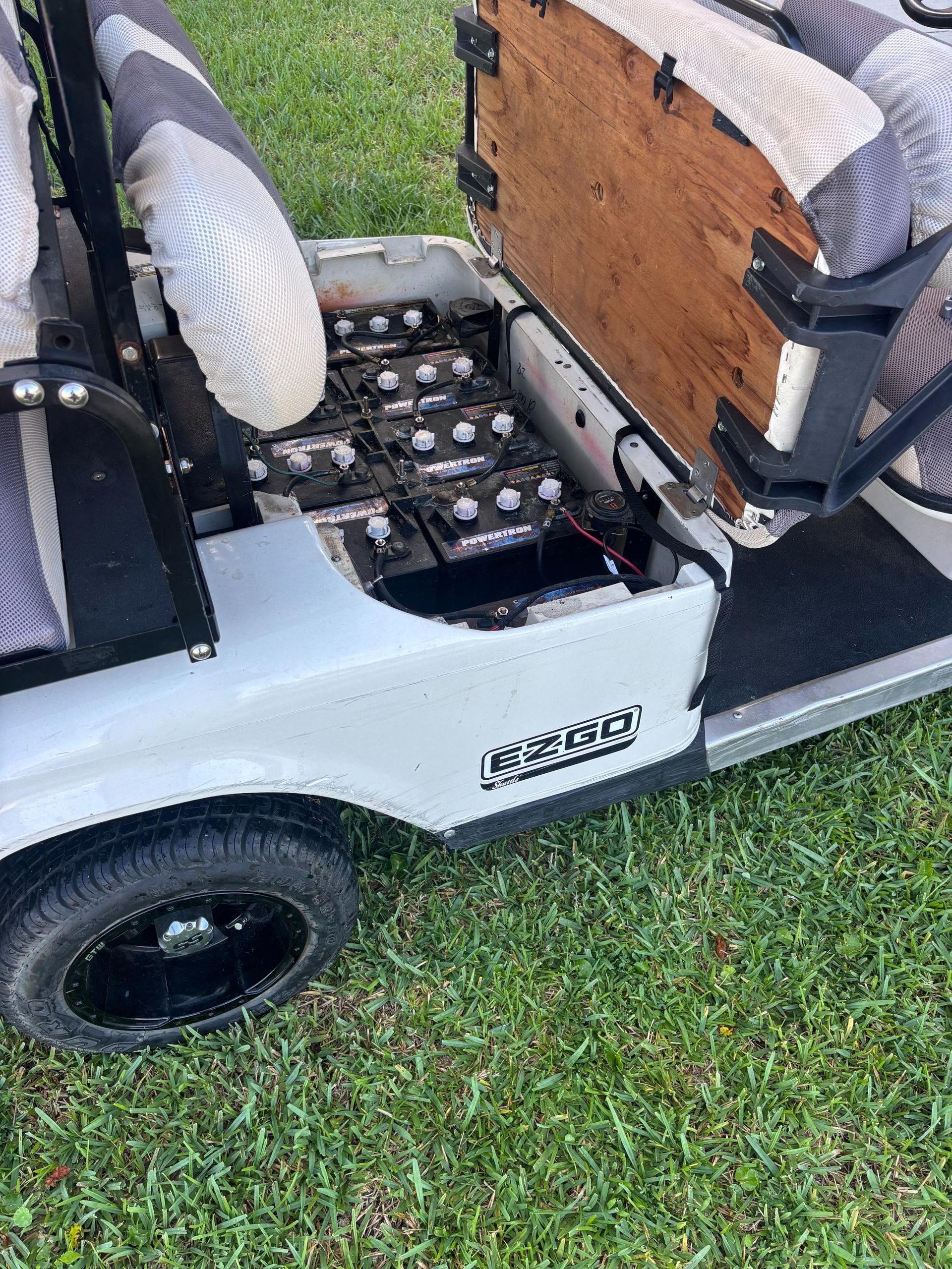 White golf cart with exposed batteries and black tires on green grass.