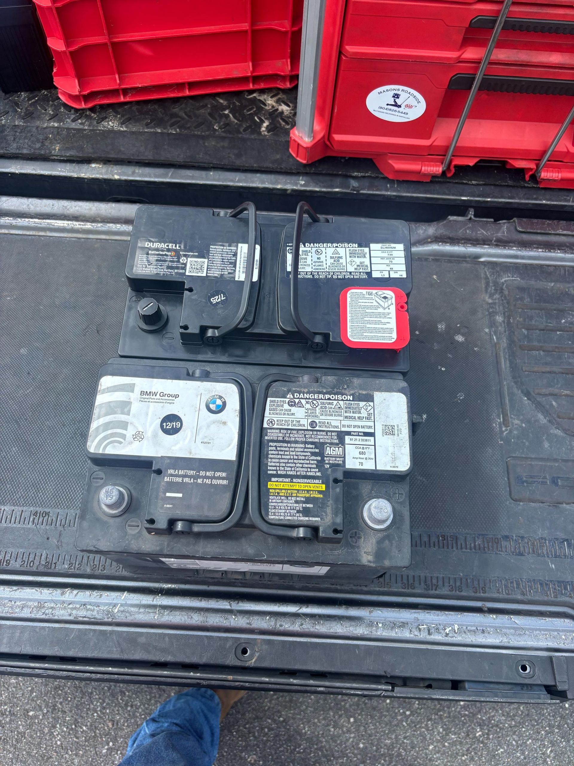 Two black car batteries stacked on a truck bed, with red crates visible.