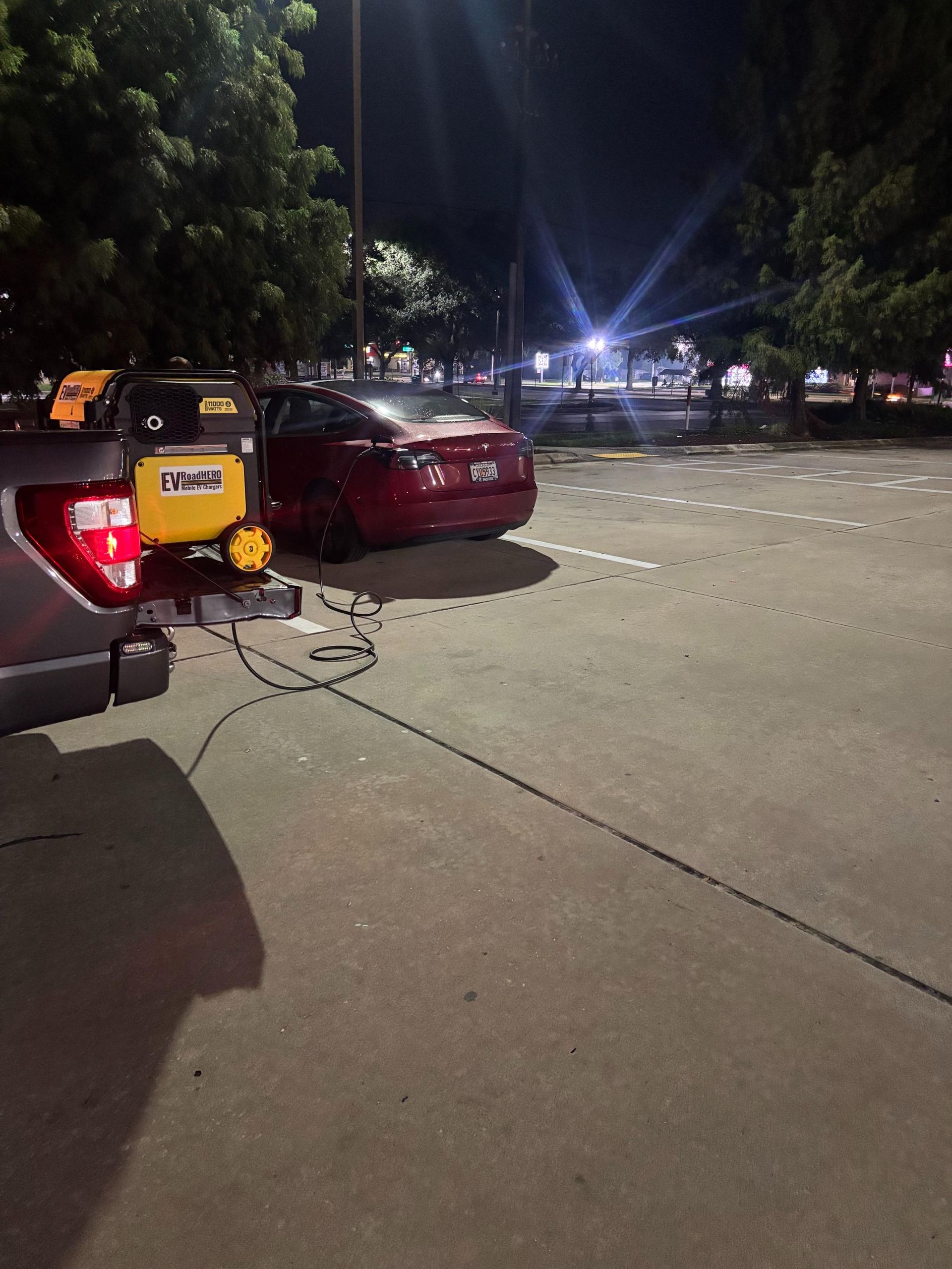 A red car parked near a yellow work vehicle in a parking lot at night.