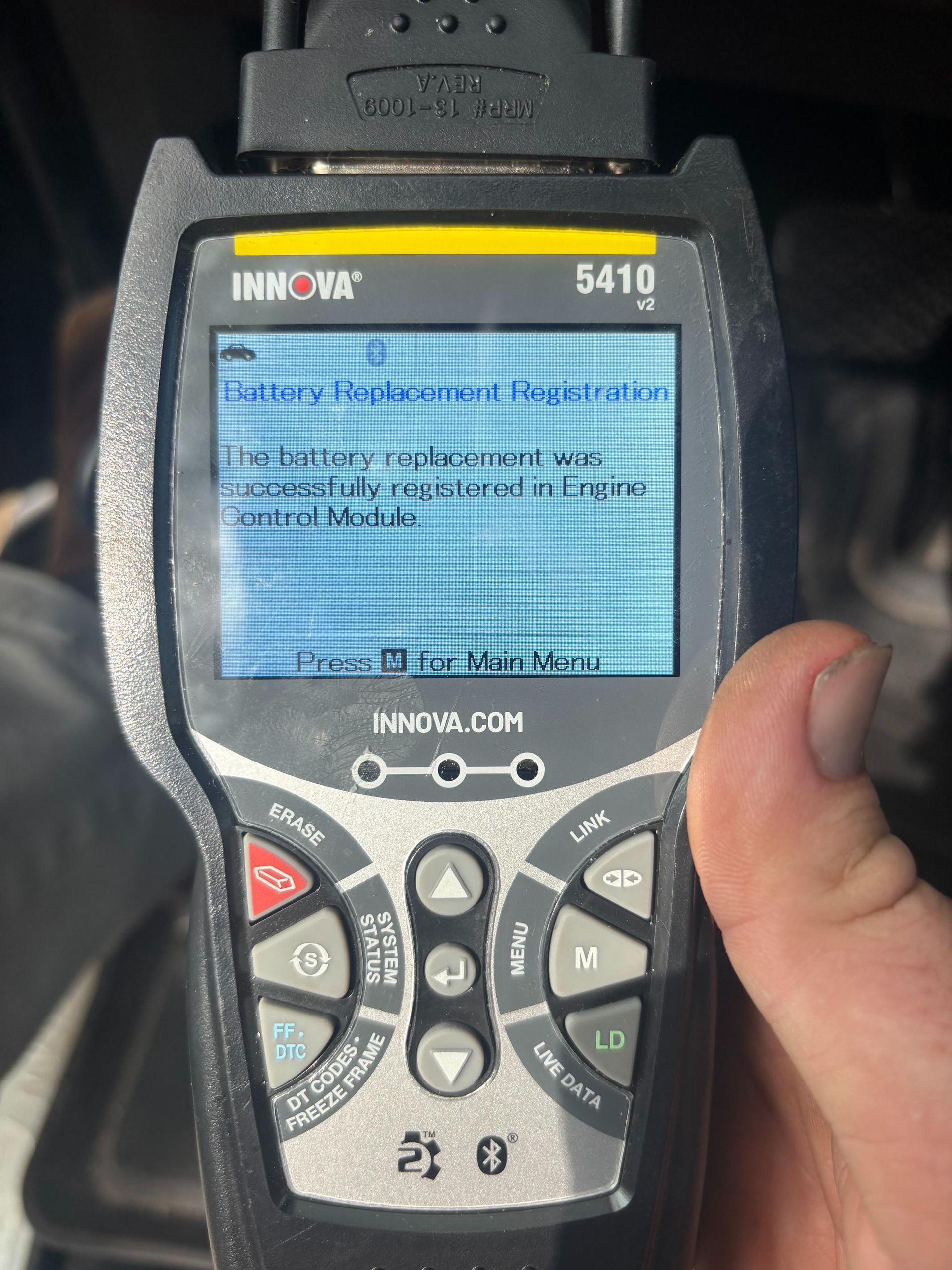 Hand holding an Innova 5410 code reader displaying a battery and ignition error message.